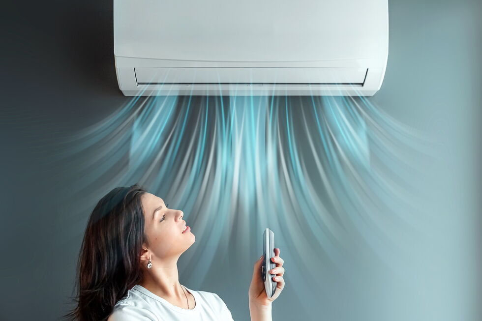 Frau steht im Luftstrom unter einer Klimaanlage