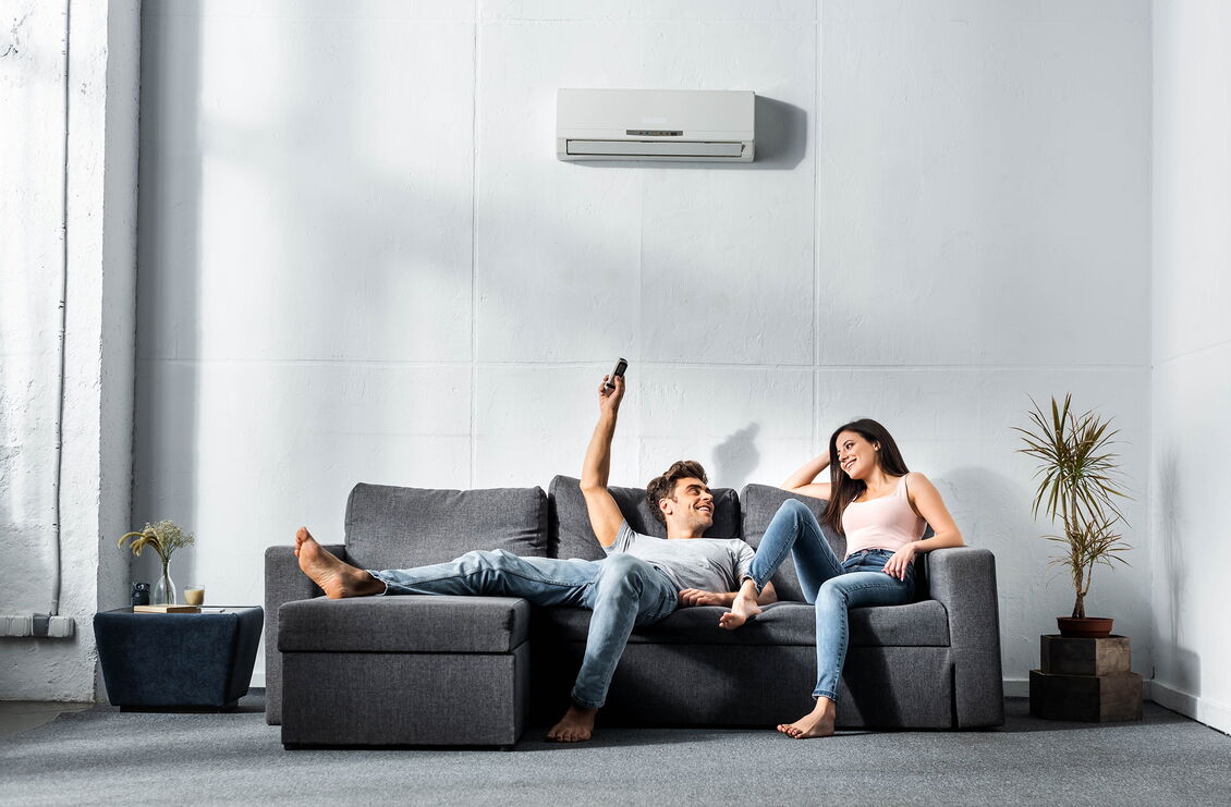 Frau und Mann auf einem Sofa bedienen ihre Klimaanlage per Fernbedienung